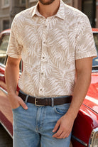 Beige short-sleeved button-down shirt with white palm leaf pattern paired with brown sport faux leather belt