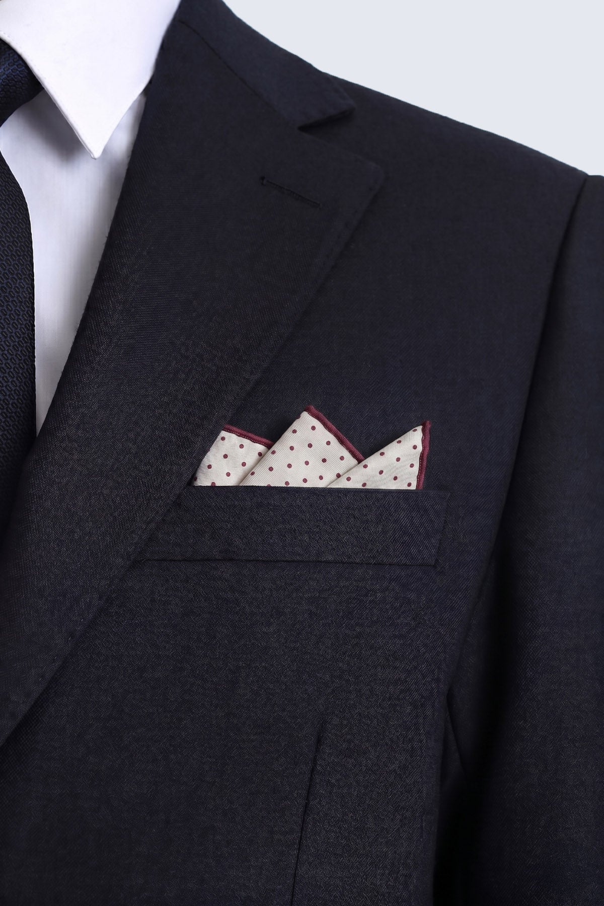 Cream-colored burgundy polka dot pocket square with dark red trim and black dots neatly folded in a suit pocket