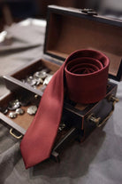 A rich burgundy silk casual 2.36 inches burgundy tie coiled on a dark wooden chest with brass hardware
