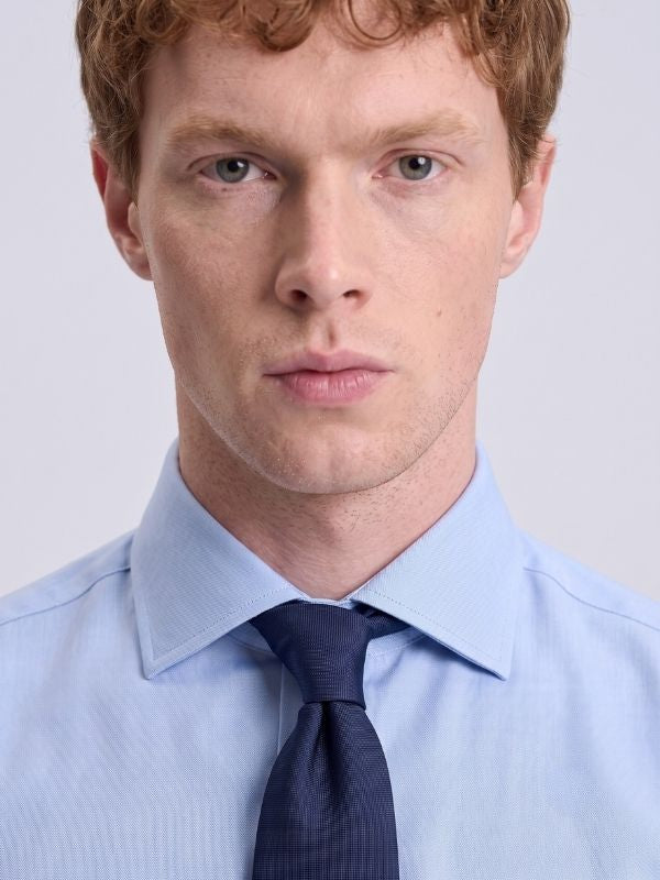 Close-up of a light blue poplin spread collar dress shirt with a navy tie