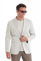 A light beige, single-breasted blazer with a subtle texture and two front flap pockets.