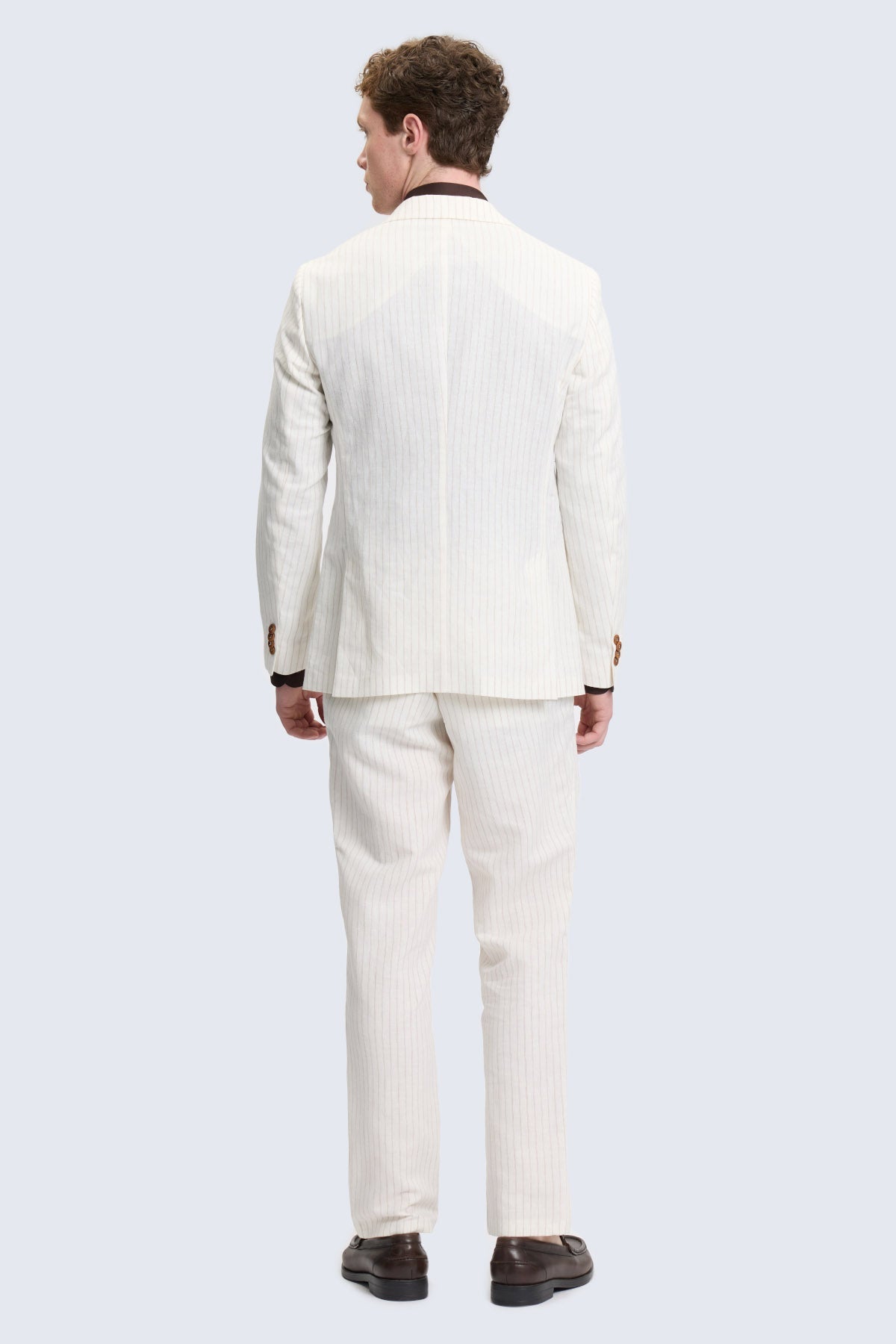 A man wearing a comfort fit ecru notch lapel striped linen-cotton suit with black collar accents and brown dress shoes