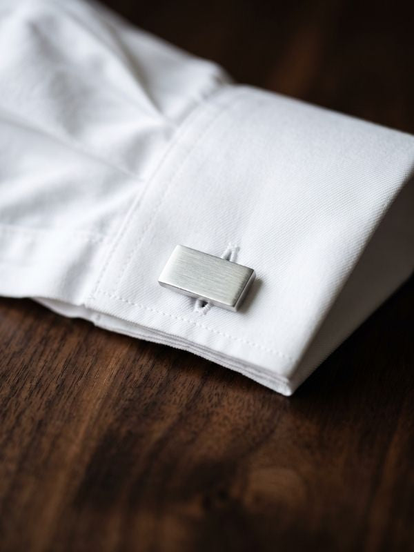 Close-up of a brushed silver cufflink fastened on a white French-cuff dress shirt sleeve