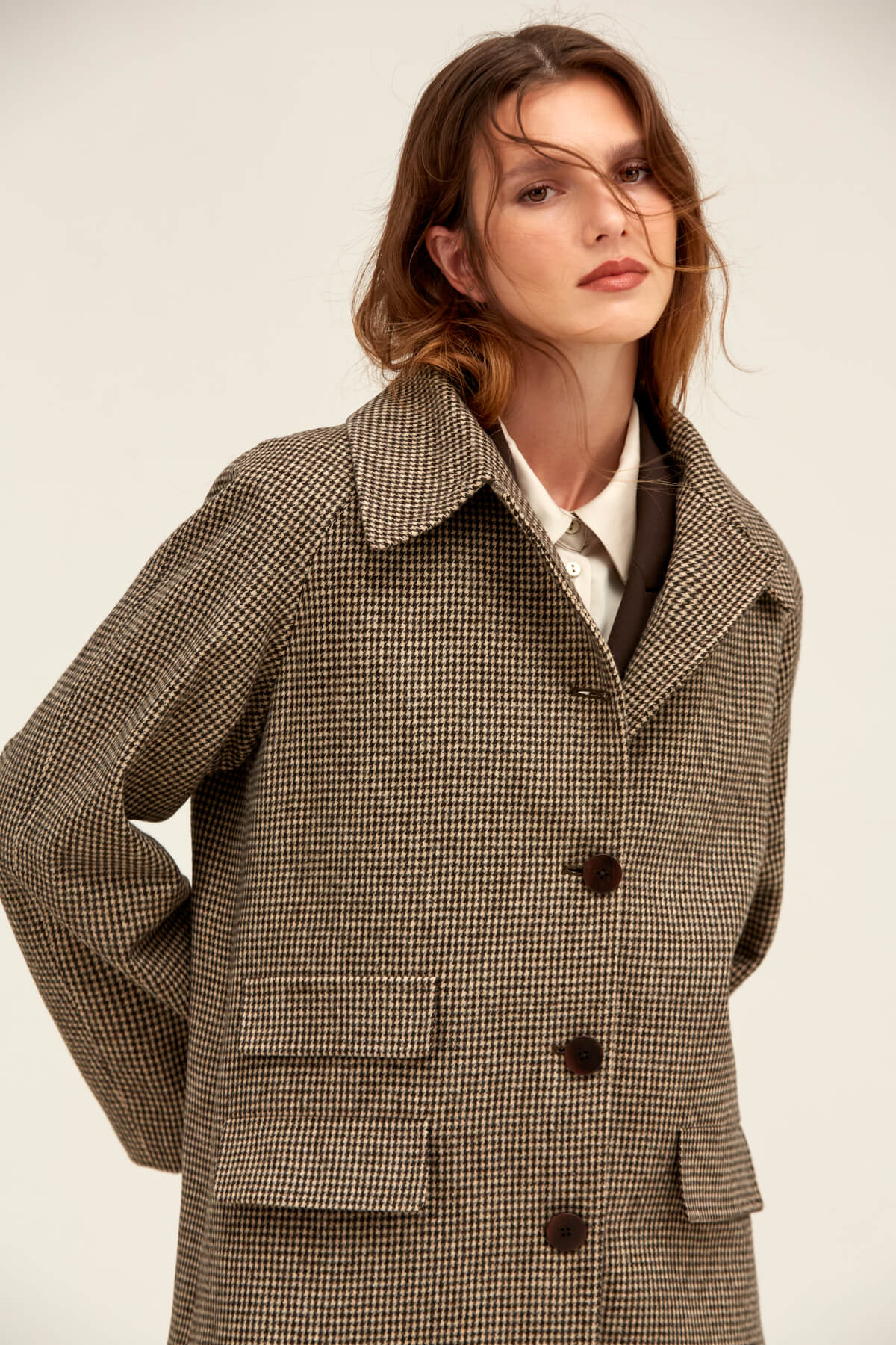 A brown and beige houndstooth wool coat with a classic collar, front buttons, and patch pockets.