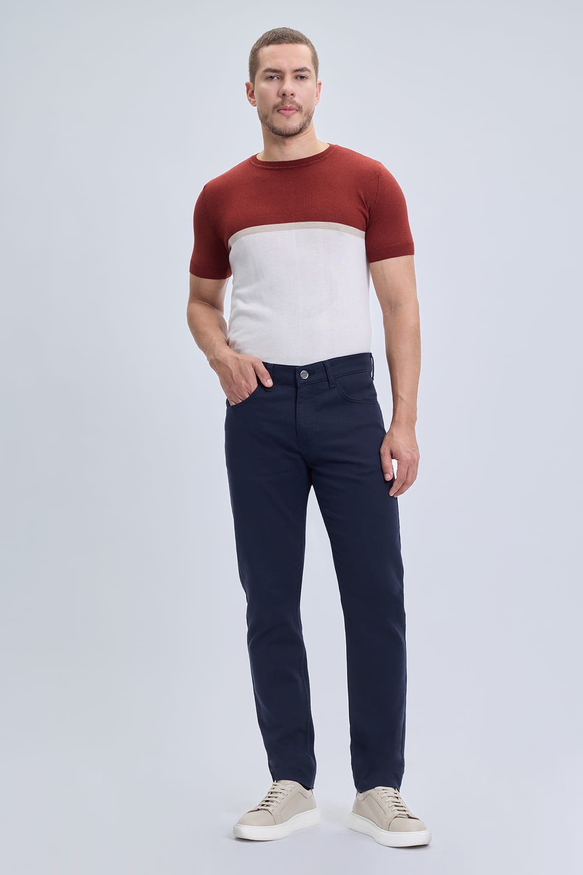 A man wearing dynamic fit navy cotton gabardine casual pants with a red and white short-sleeved knit tee in smart casual style