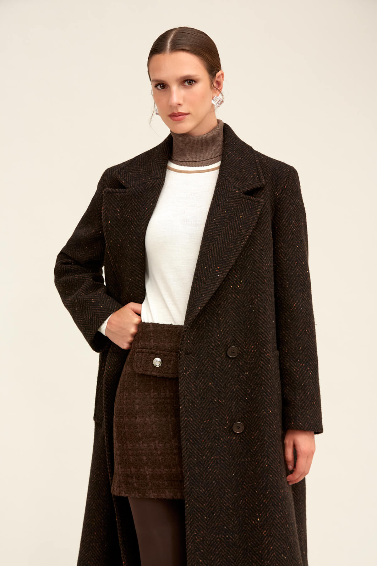A dark brown herringbone wool coat with a double-breasted front and matching buttoned pocket.