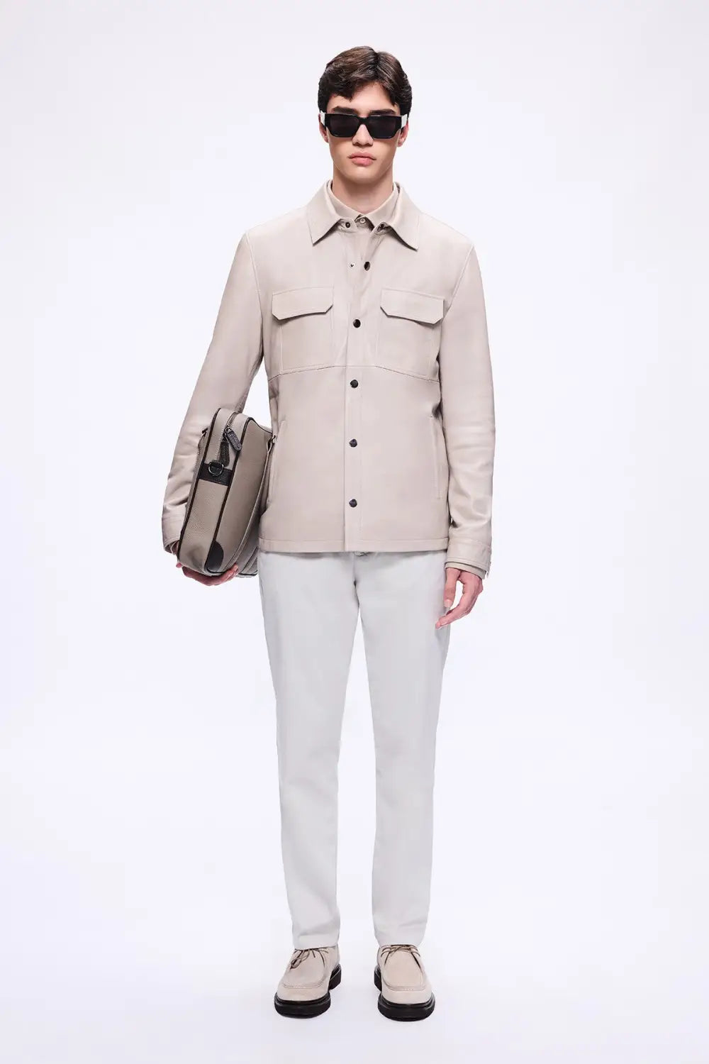 Model wearing beige shirt jacket with light grey trousers and designer bag showcasing relaxed tailoring