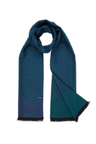 A deep teal scarf with a subtle gradient to navy blue at the bottom, featuring black fringed edges and a small brand tag.