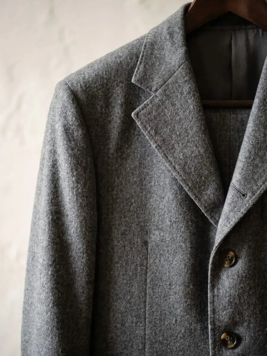 Close-up of medium grey wool flannel suit jacket fabric showing soft brushed napped surface with peak lapel and button detail