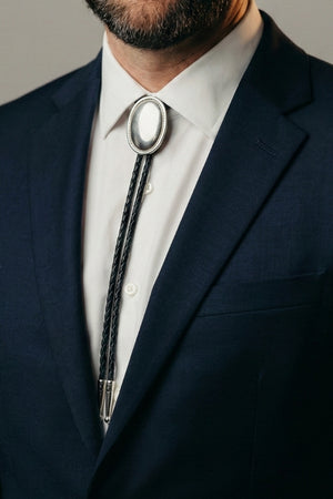 Man wearing a silver bolo tie clasp with a navy suit