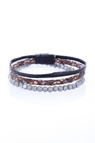 A layered bracelet featuring a black leather band, a brown lace-patterned strap with metallic accents, and a row of gray faceted beads.
