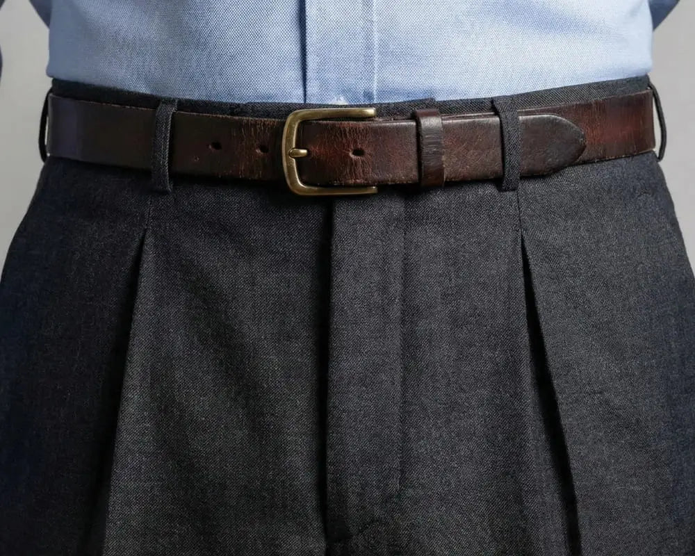 Close-up detail of charcoal gray single-pleated wool trousers showing the waistband and pleat construction
