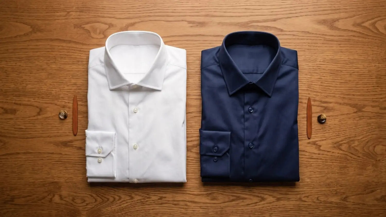 White pure cotton dress shirt and navy cotton blend dress shirt folded side by side on a wooden surface