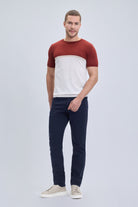 A man wearing a regular fit brick crew neck t-shirt with red and white color blocks paired with dark navy trousers