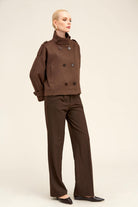 Brown double-breasted trench coat with structured shoulders and matte fabric.