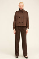 Brown double-breasted trench coat with black buttons and belted cuffs.