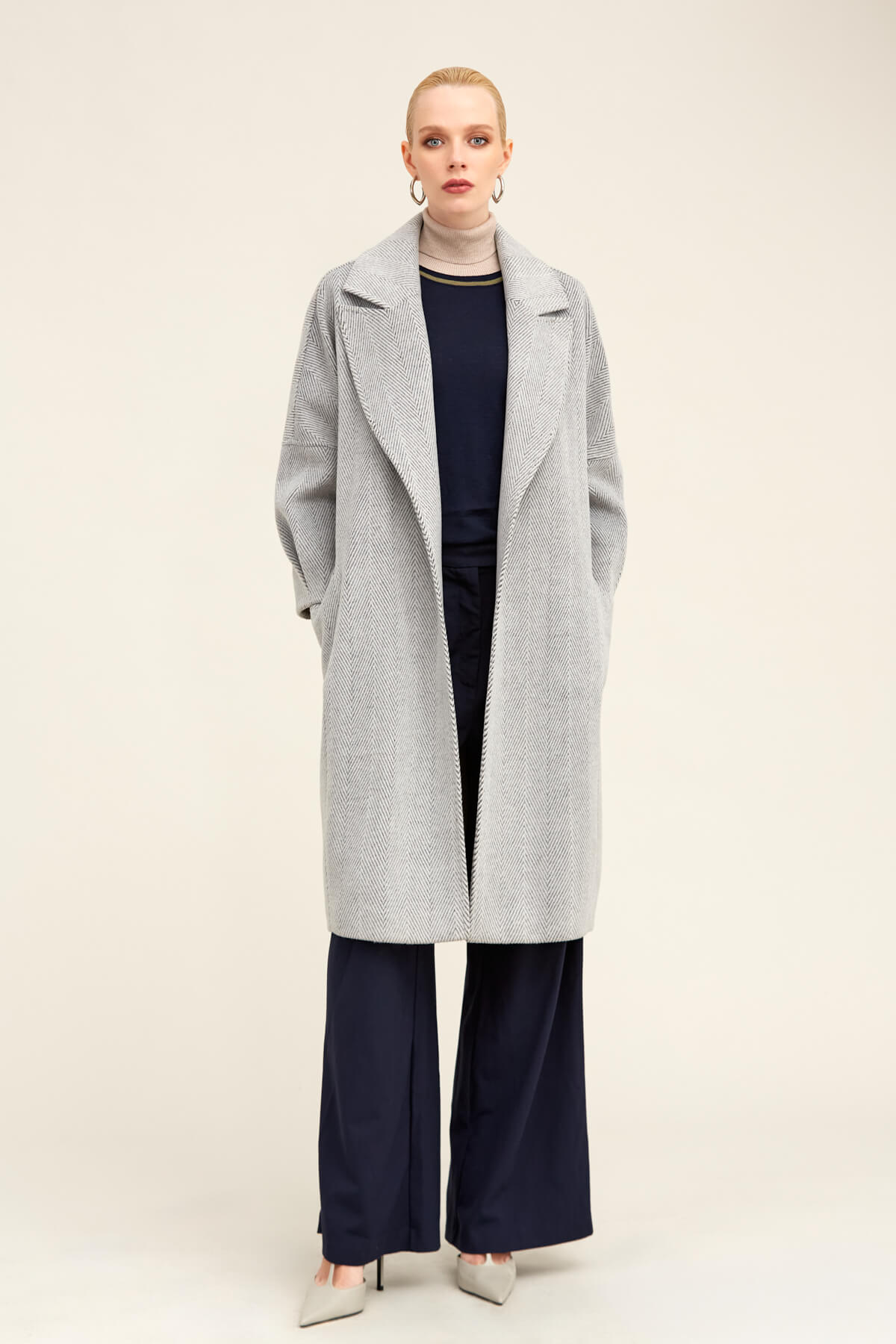 A long, light gray herringbone-patterned wool coat with a classic collar and wide sleeves.