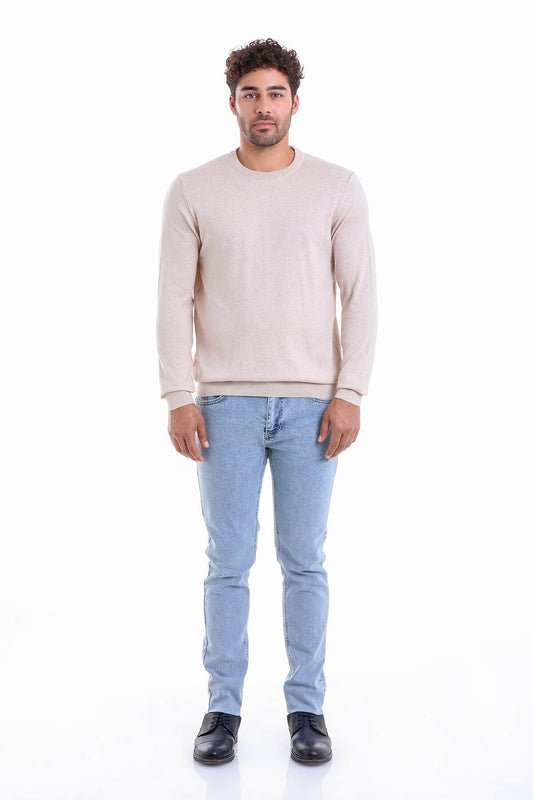 A man wearing a soft beige long-sleeved sweater with a crew neck and light blue denim jeans.