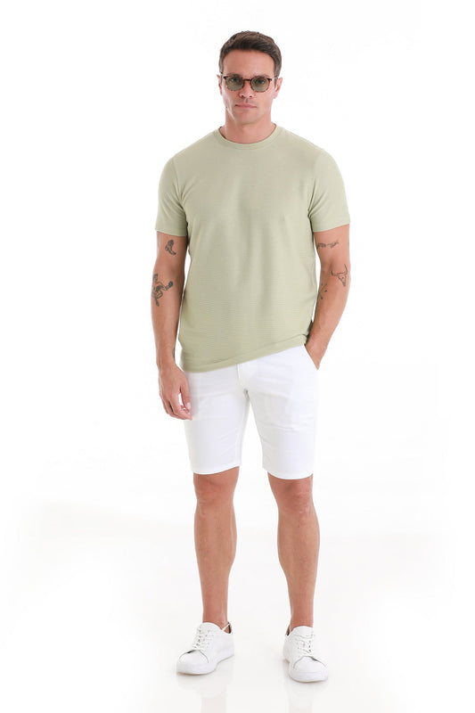 A man wearing a light green, short-sleeved crew neck t-shirt paired with white shorts and white sneakers.