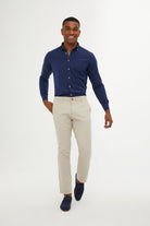 A man wearing a navy blue long-sleeved button-down shirt with white buttons, paired with light beige chinos and dark navy loafers.