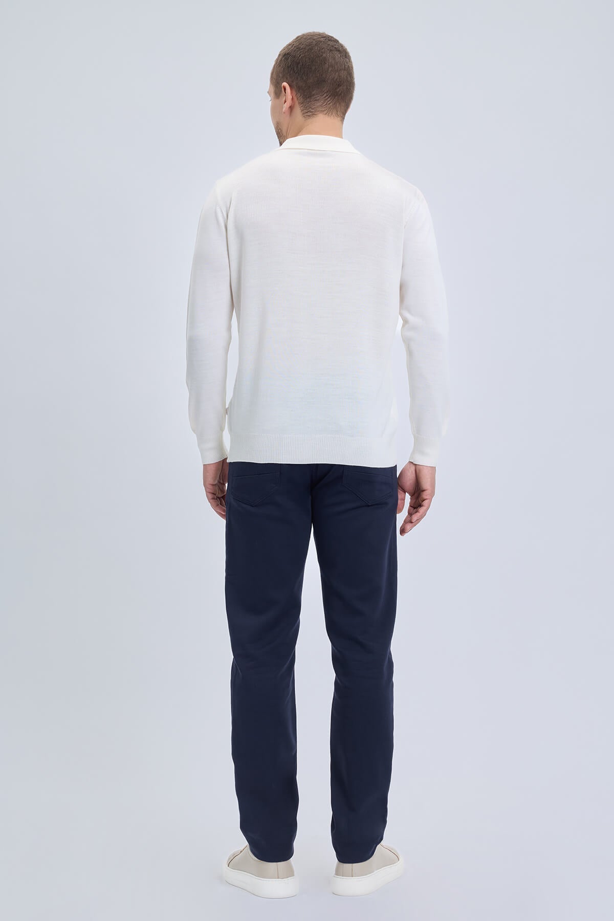 A man wearing a white regular fit johnny polo sweater in wool blend with dark navy trousers