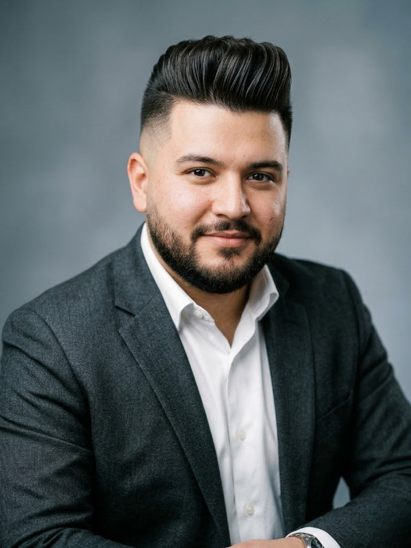 Man with a round face shape wearing a high fade pompadour haircut and a charcoal suit
