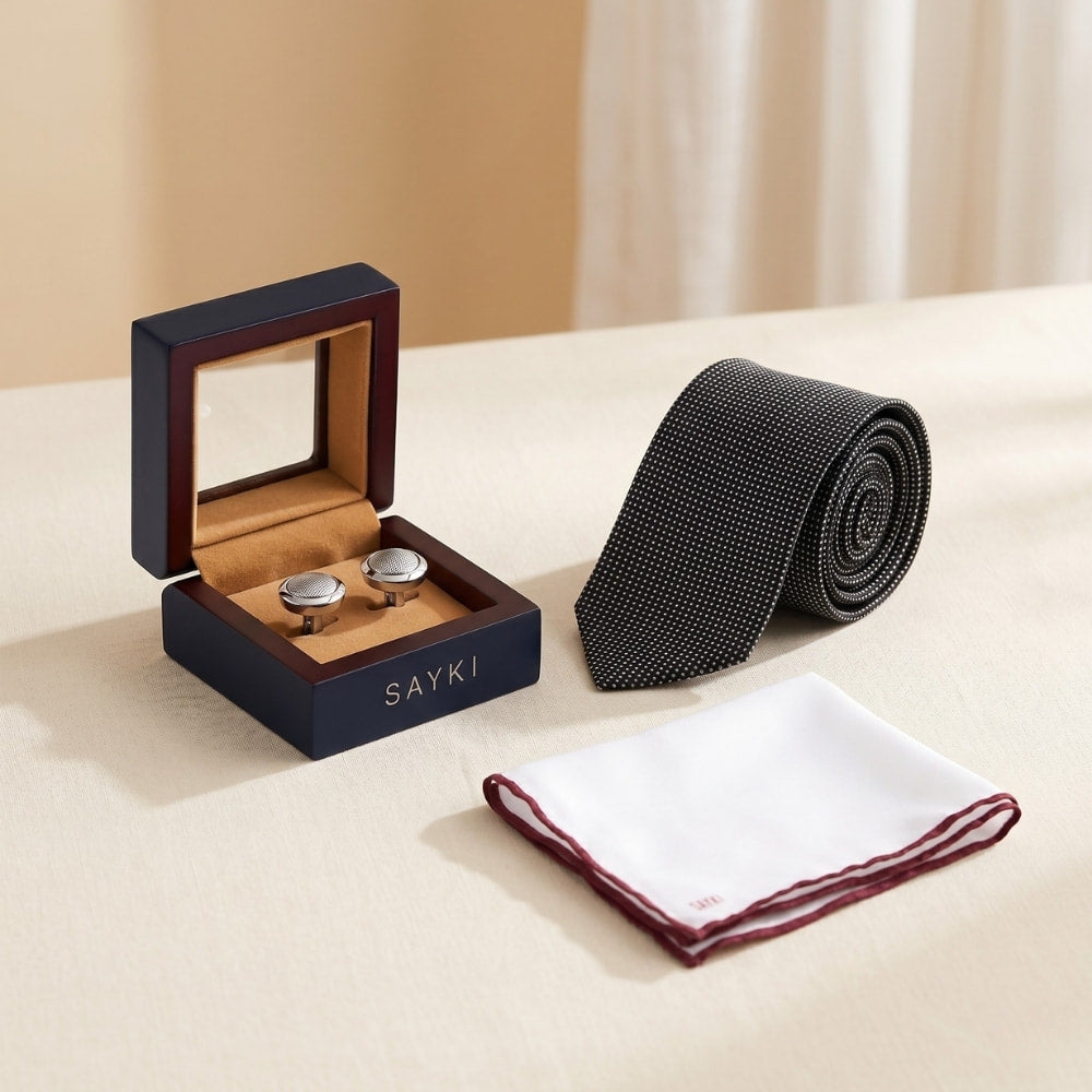 Cufflinks in a wooden box, black tie, and white pocket square on a beige surface with 'SAYKI' branding.