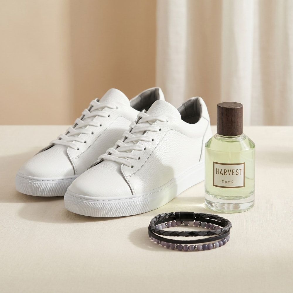 White sneakers, a bottle of 'Harvest' cologne, and a bracelet on a light surface.