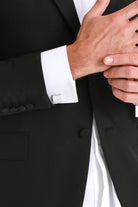 Silver rectangular cufflink with a minimalist design, fastened to the white shirt cuff of a black suit.