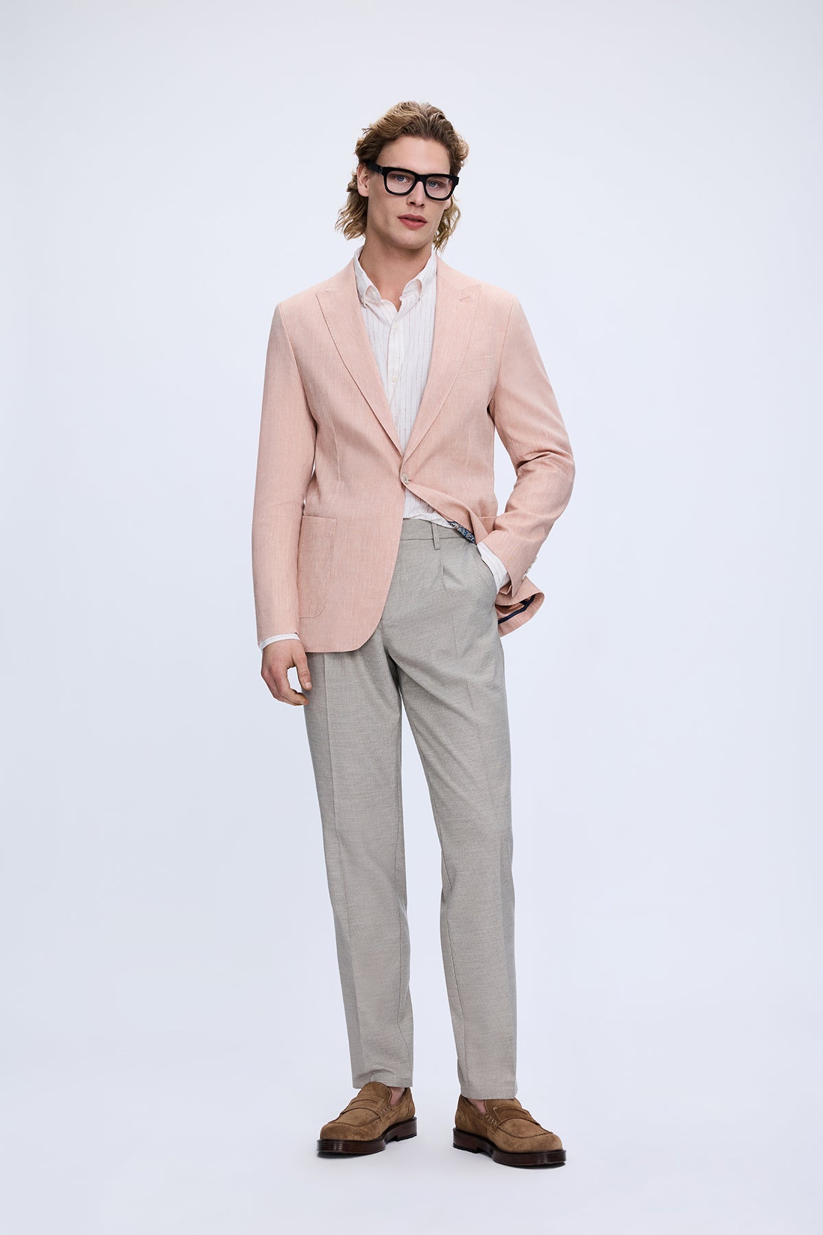 A man wearing a slim fit light pink peak lapel linen casual blazer with matching tailored trousers