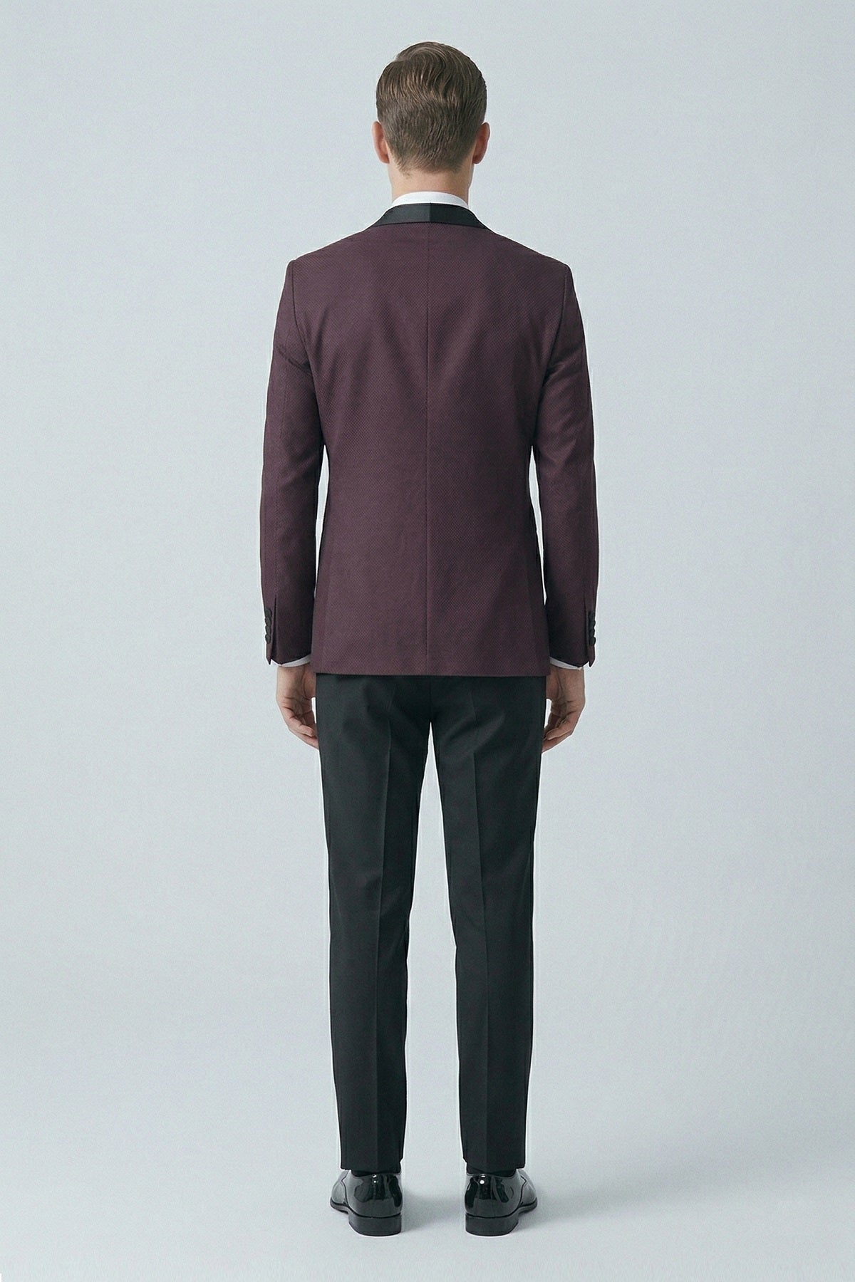 Slim fit classic tuxedo with a burgundy peak lapel jacket featuring black satin collar and matching cuffs worn with dark trousers