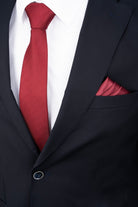 A rich crimson silk tie with a subtle textured weave, neatly knotted against a crisp white shirt and black suit.