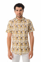 A men’s short-sleeved button-up shirt in a light beige base with a repeating pattern of yellow and dark gray tropical leaves.