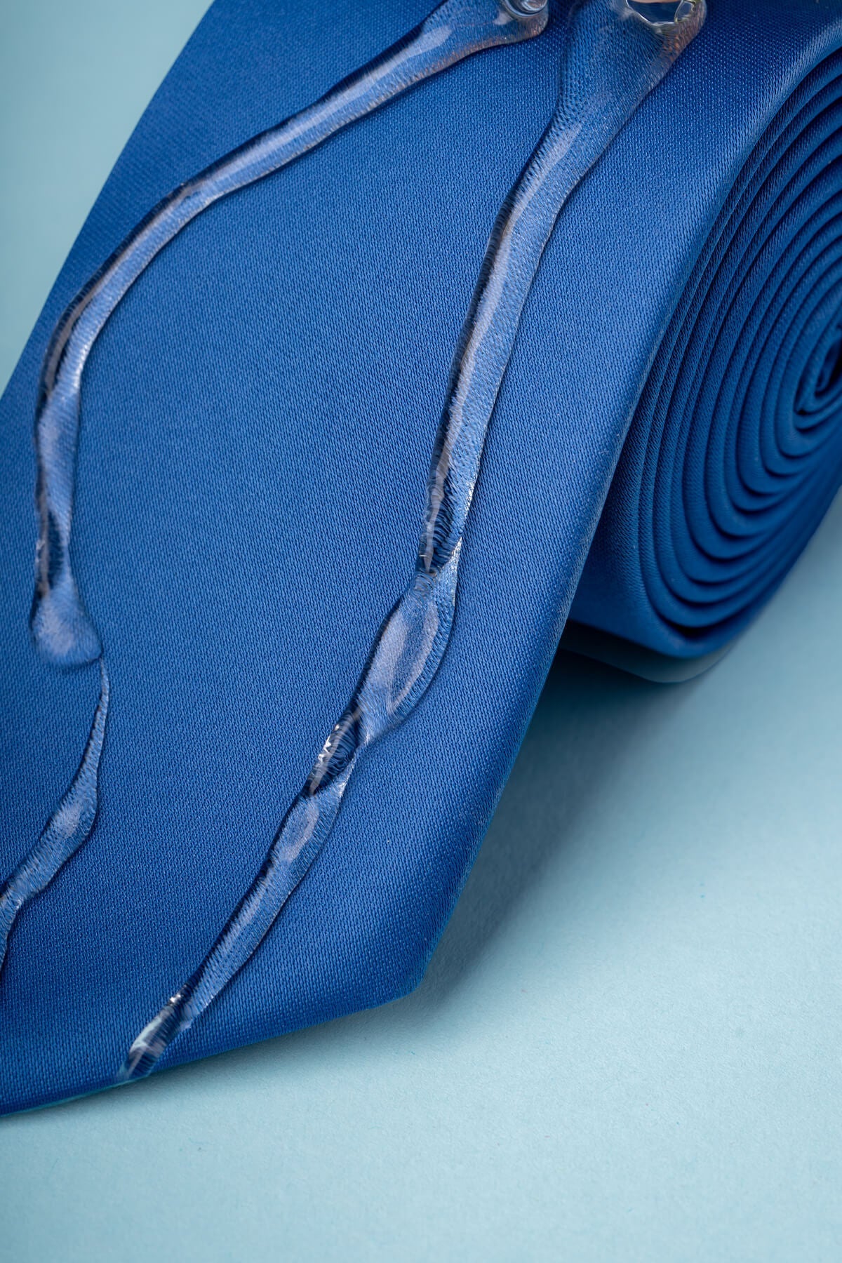 A vibrant royal blue silk tie featuring a subtle, translucent design resembling flowing liquid or glass strands.