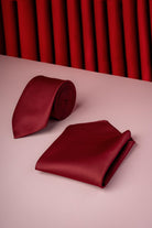 A rich burgundy silk tie and matching pocket square set, elegantly arranged on a soft pink surface.
