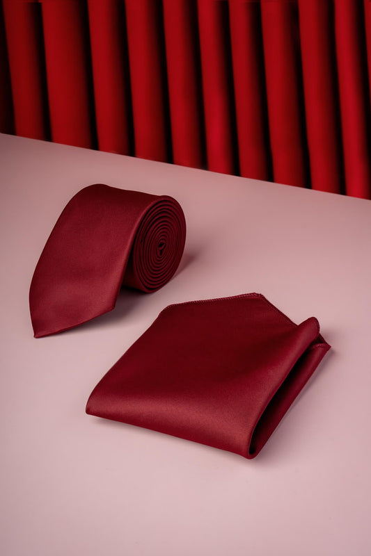 A rich burgundy silk tie and matching pocket square set, elegantly arranged on a soft pink surface.