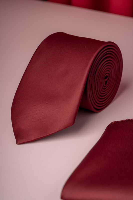 A rich burgundy satin tie, neatly rolled and displayed alongside a matching pocket square.